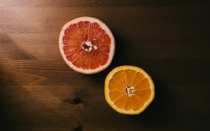 two orange and grapefruit halves on brown wooden surface